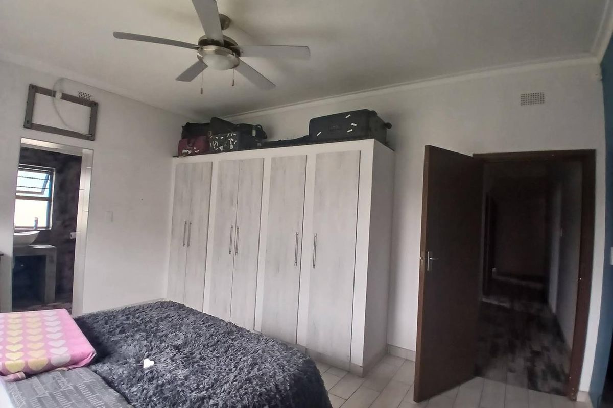 A bedroom featuring built-in wardrobes, tiled flooring, and a ceiling fan, with an adjacent en-suite bathroom visible through the doorway.