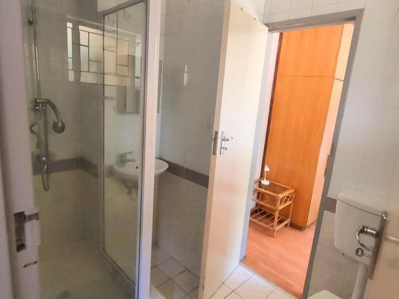 A functional bathroom featuring a shower enclosure, pedestal basin, and toilet with tiled finishes, requiring some cosmetic updates to improve its overall condition.