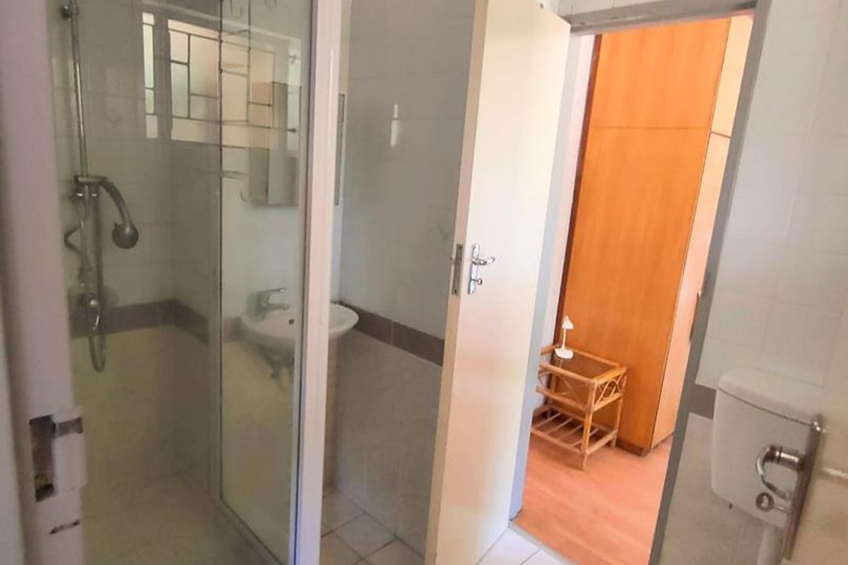 A functional bathroom featuring a shower enclosure, pedestal basin, and toilet with tiled finishes, requiring some cosmetic updates to improve its overall condition.
