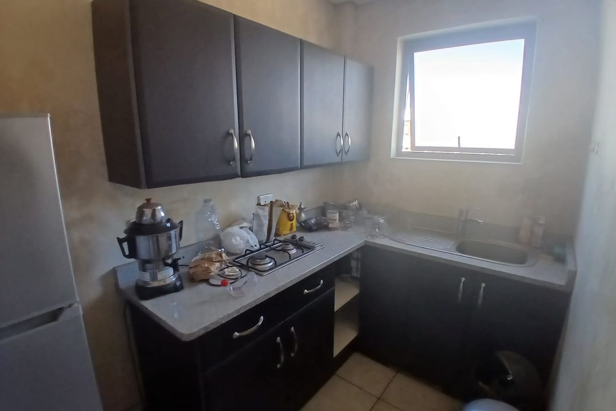 Compact kitchen featuring dark cabinetry, stone countertops, a built-in gas hob, and a stainless steel sink with a window for natural light.