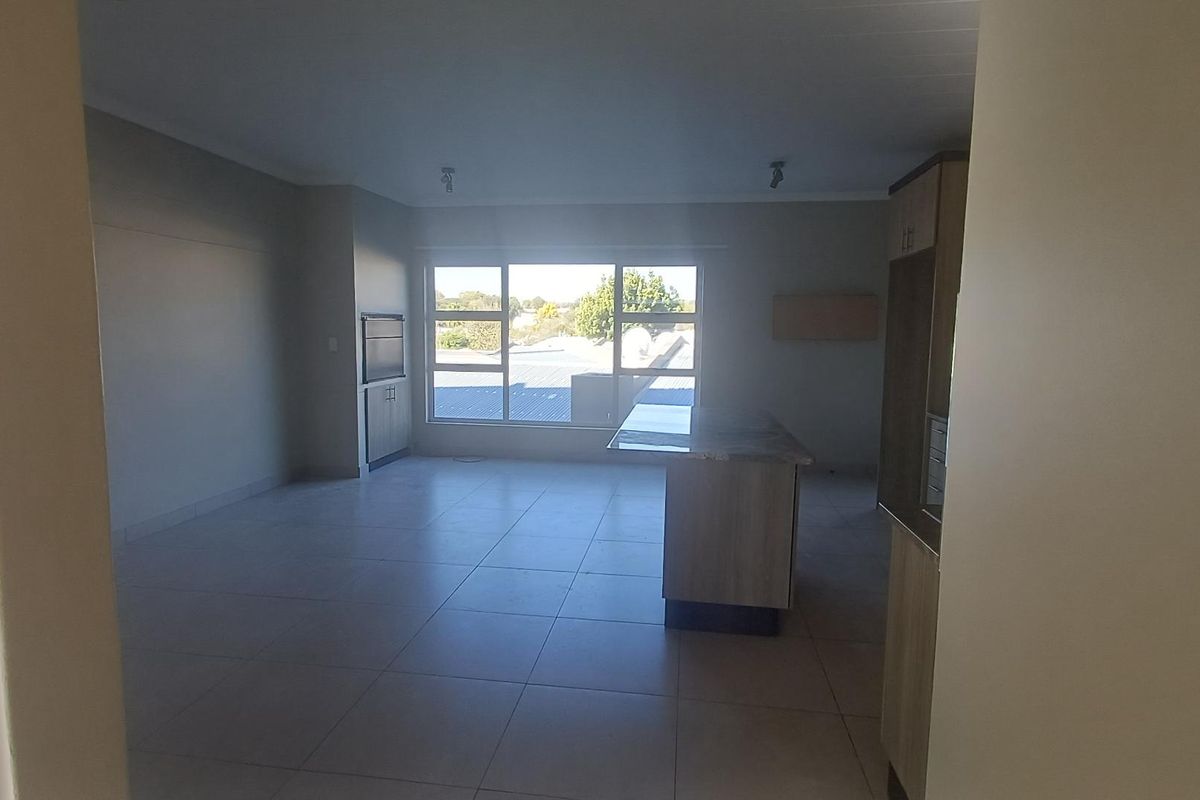 Spacious open-plan living and kitchen area featuring tiled flooring, a central kitchen island, and large windows providing ample natural light.