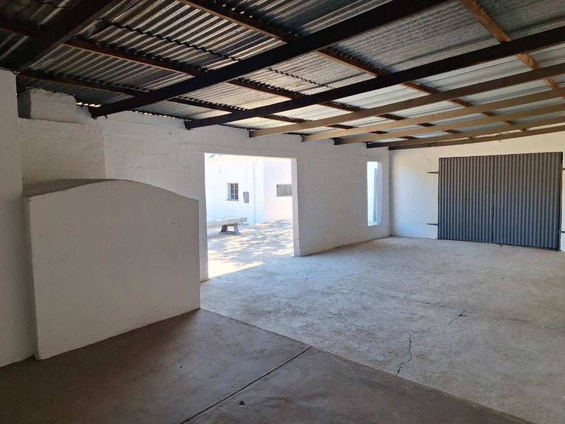 Spacious garage featuring a corrugated metal roof, exposed timber rafters, and a concrete floor with direct access to an outdoor area.