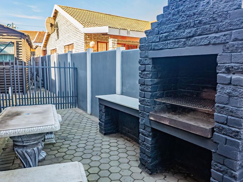 Outdoor patio area featuring a built-in brick braai, paved flooring, and secure boundary walling, ideal for outdoor entertaining.