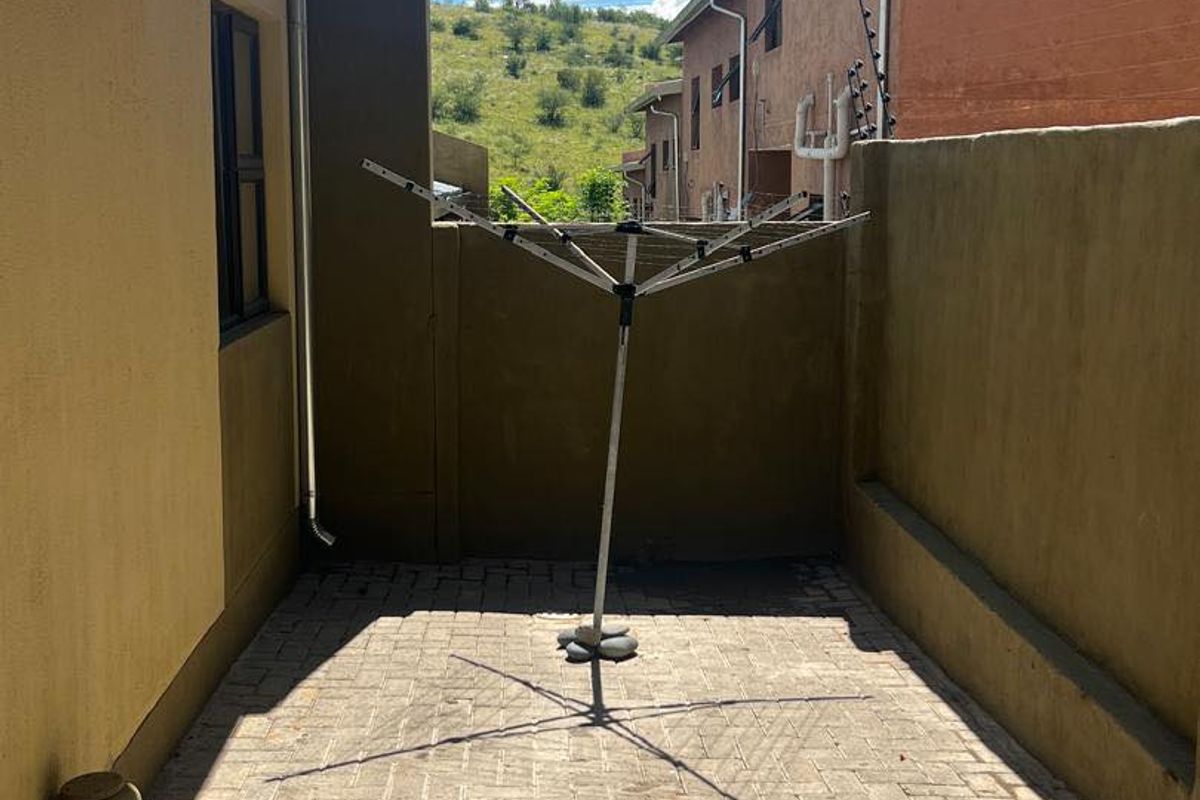 A paved rear courtyard area featuring an exterior wall-mounted geyser and a fixed rotary washing line, providing a functional outdoor utility space.