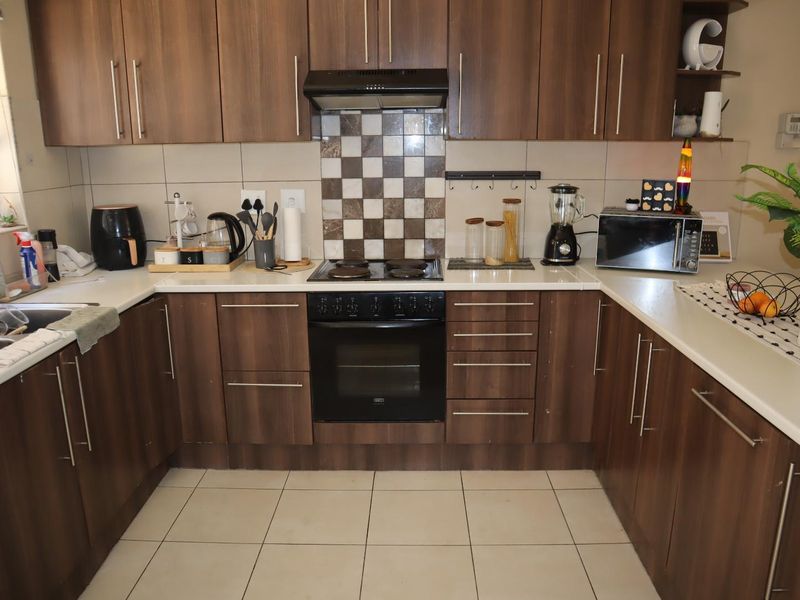 A functional U-shaped kitchen featuring dark wood-look cabinetry, tiled splashbacks, built-in oven and hob, and ample counter space.