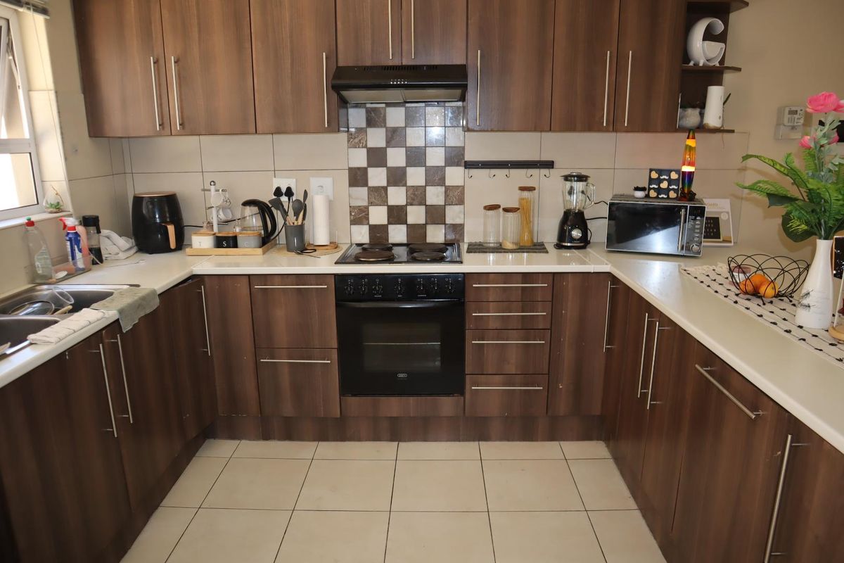 A functional U-shaped kitchen featuring dark wood-look cabinetry, tiled splashbacks, built-in oven and hob, and ample counter space.