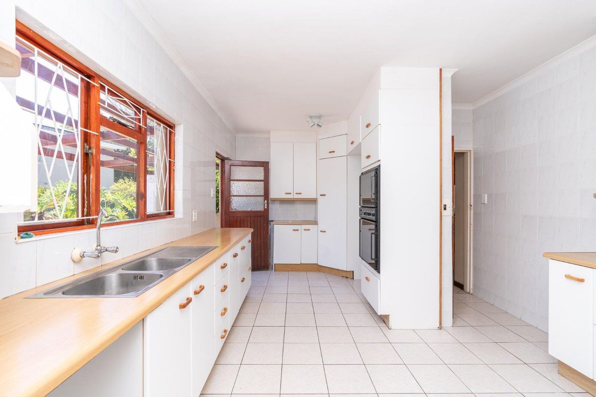 A functional kitchen featuring white built-in cabinetry, laminate countertops, a double stainless steel sink, and tiled finishes throughout.