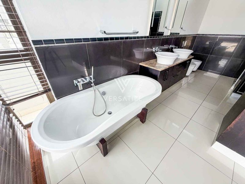 Modern bathroom featuring a freestanding bathtub, double vessel sink vanity, and dark tiled wall accents with neutral floor tiles.