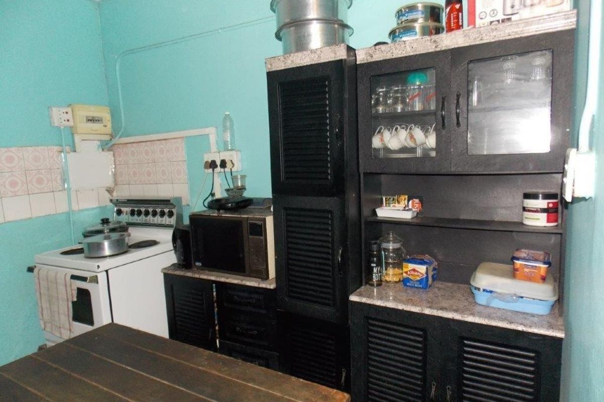 A compact kitchen featuring dark built-in cabinetry, a freestanding stove, and tiled splashback, requiring cosmetic updates to modernize the space.