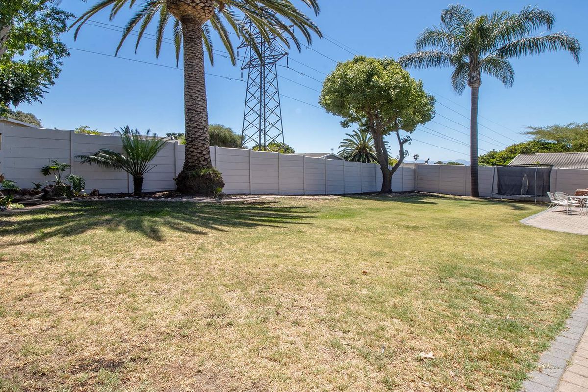 Spacious rear garden featuring a large lawn area, paved patio section, and perimeter boundary wall with mature palm trees.