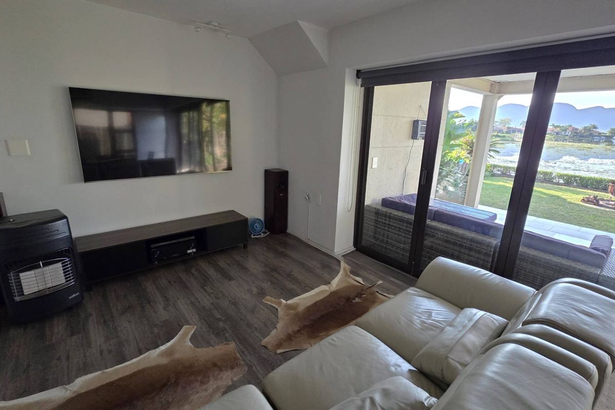 A bright living room featuring laminate flooring and large sliding glass doors that provide seamless access to the patio and scenic water views.