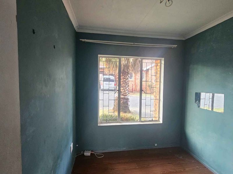 An empty bedroom featuring laminate flooring, security bars on the window, and coving, requiring cosmetic updates to the wall finishes.
