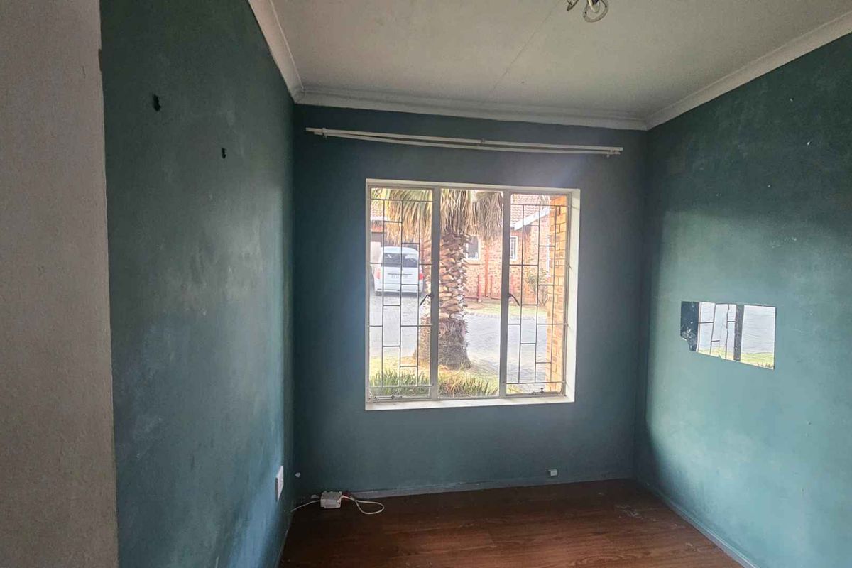 An empty bedroom featuring laminate flooring, security bars on the window, and coving, requiring cosmetic updates to the wall finishes.