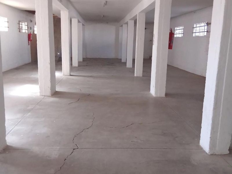 An expansive, open-plan industrial utility space featuring concrete flooring, structural support columns, and security-barred windows, suitable for storage or workshop use.