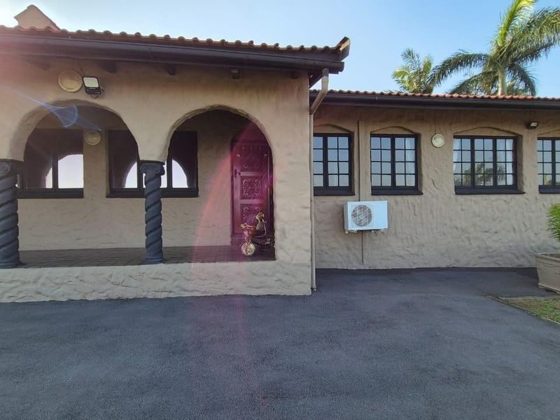 Front elevation of a house featuring an arched porch with decorative columns, grid-style windows, and an asphalt driveway.