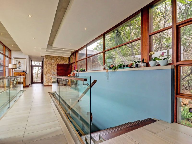 Spacious hallway featuring a modern glass balustrade, stone feature wall, and large timber-framed windows overlooking the surrounding garden.