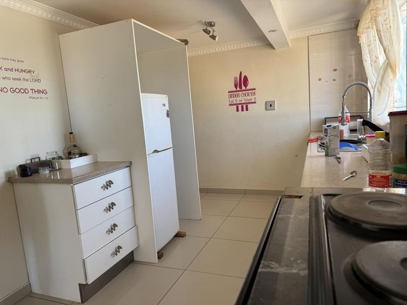 A functional kitchen featuring tiled flooring, built-in cabinetry with laminate countertops, a stainless steel sink, and an integrated electric hob.