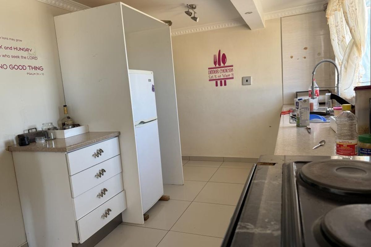 A functional kitchen featuring tiled flooring, built-in cabinetry with laminate countertops, a stainless steel sink, and an integrated electric hob.