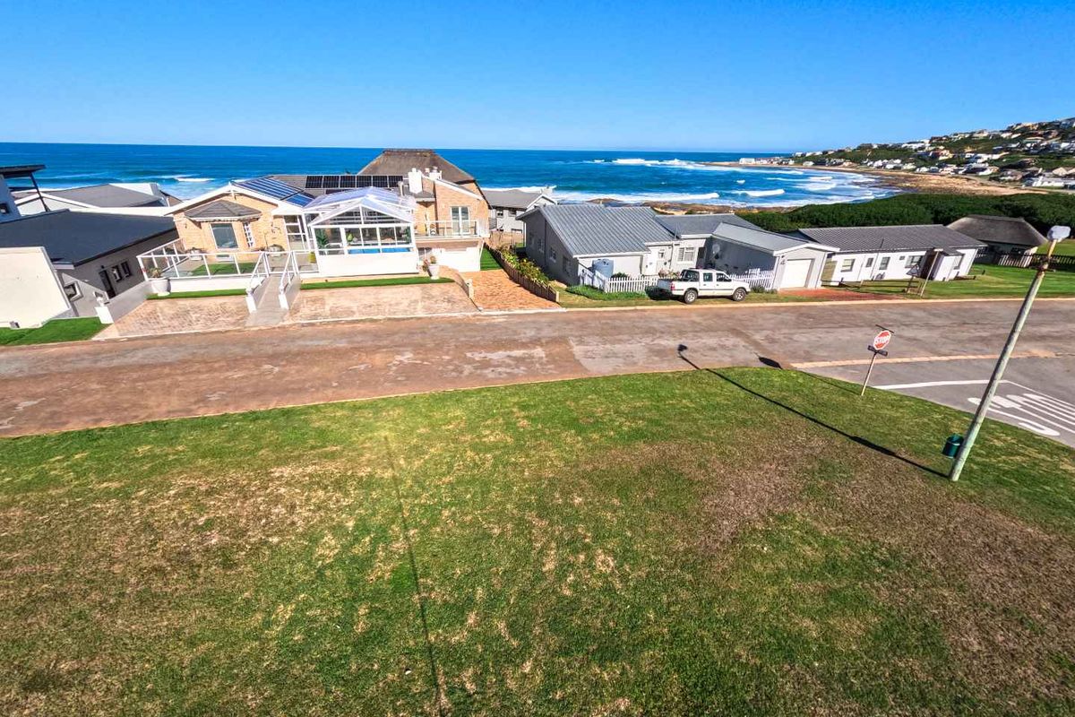 An elevated aerial view of a coastal residential property featuring a paved driveway, landscaped lawn, and proximity to the ocean.