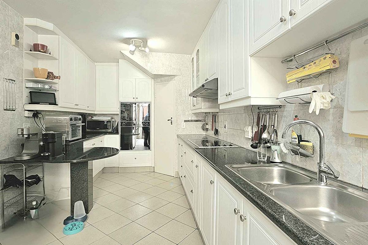 A functional kitchen featuring white cabinetry, dark granite countertops, a double stainless steel sink, built-in oven, and a glass-top hob.