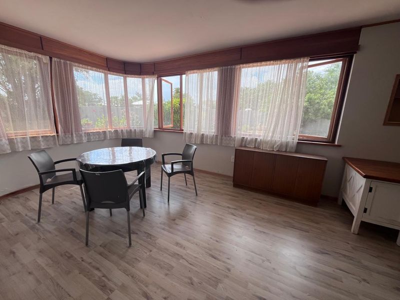 A bright dining area featuring timber-framed windows, laminate flooring, and built-in timber pelmets, offering a pleasant view of the garden.