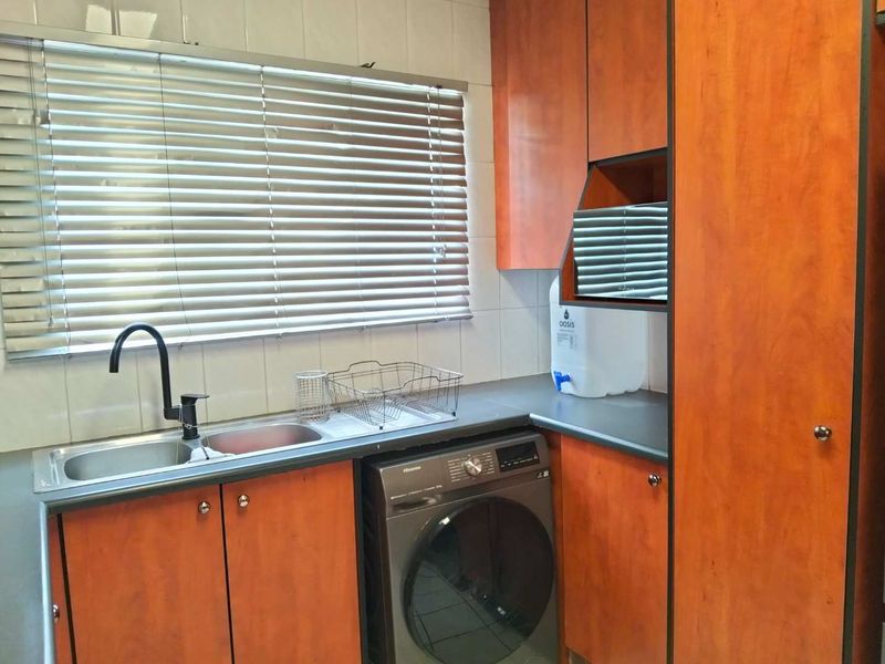 A functional laundry area featuring built-in wooden cabinetry, a stainless steel sink, and tiled backsplash, providing practical utility space for the home.