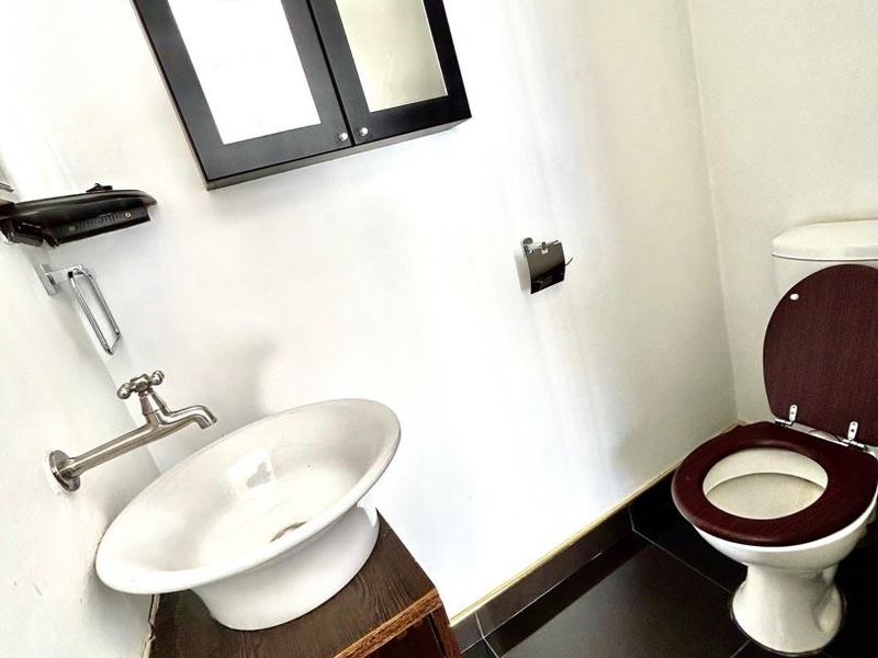 A compact bathroom featuring a vessel sink on a dark wood vanity, a wall-mounted faucet, and a matching toilet with dark wood seat.