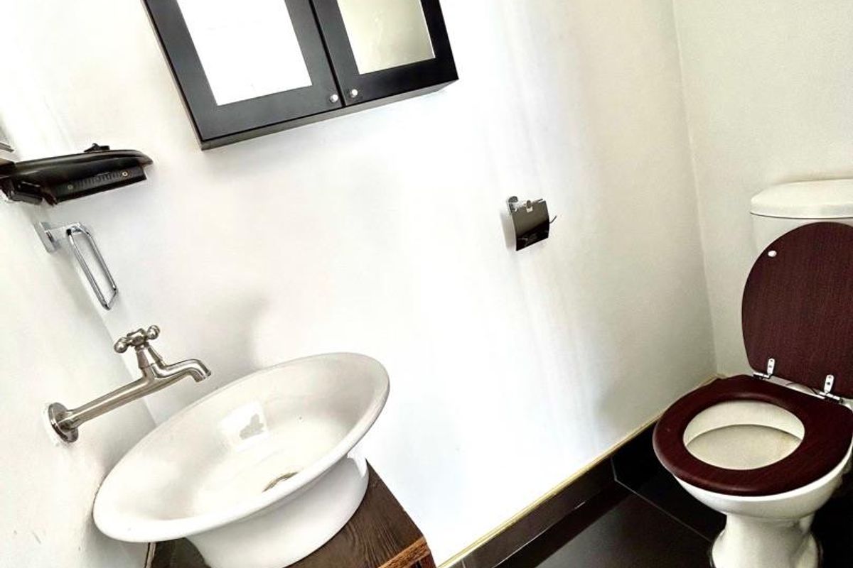 A compact bathroom featuring a vessel sink on a dark wood vanity, a wall-mounted faucet, and a matching toilet with dark wood seat.