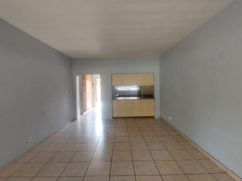 An empty open-plan living and kitchen area featuring tiled flooring and dated built-in cabinetry, offering a blank canvas for renovation.