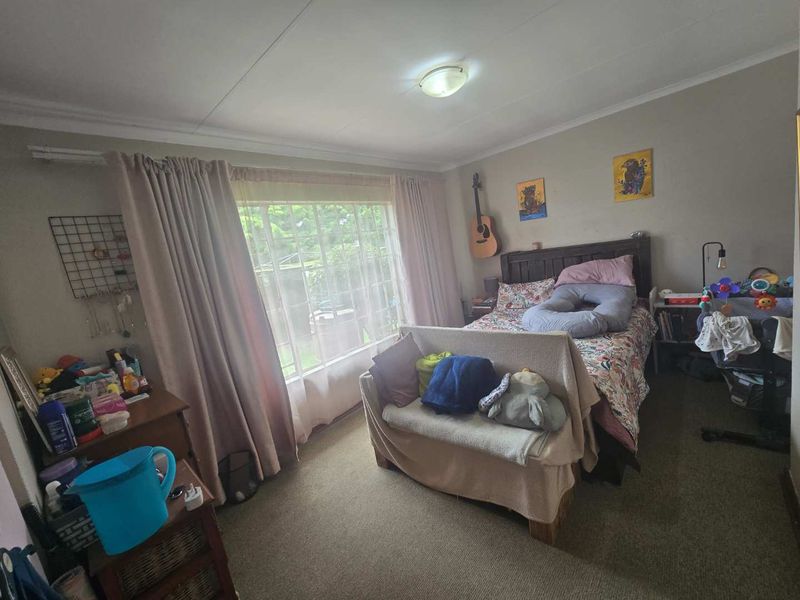 A standard bedroom featuring carpeted flooring, a large window with curtains, and a central ceiling light fixture.