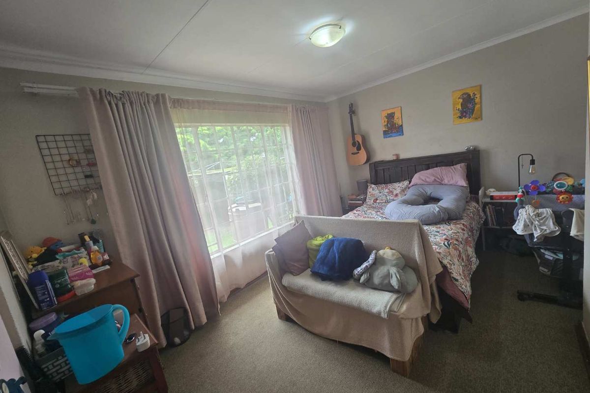 A standard bedroom featuring carpeted flooring, a large window with curtains, and a central ceiling light fixture.