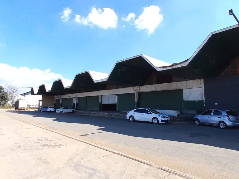 Industrial warehouse facility featuring a distinctive sawtooth roof design, concrete loading apron, and multiple roller shutter access points.