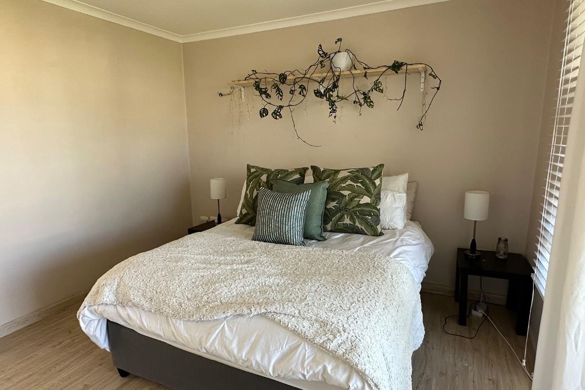 A well-maintained bedroom featuring light-toned laminate flooring, neutral wall finishes, and venetian blinds for natural light control.