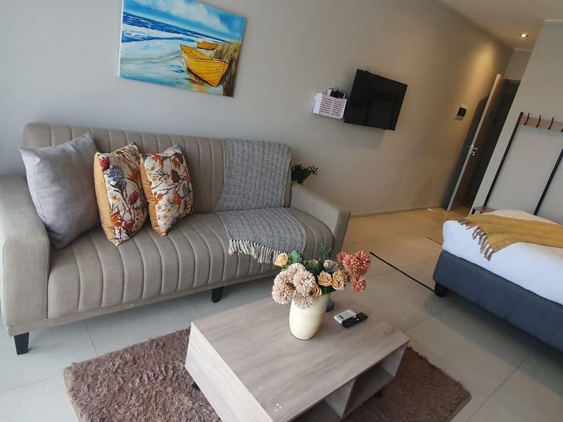 An open-plan living and sleeping area featuring neutral tiled flooring, modern recessed lighting, and a functional layout suitable for compact apartment living.