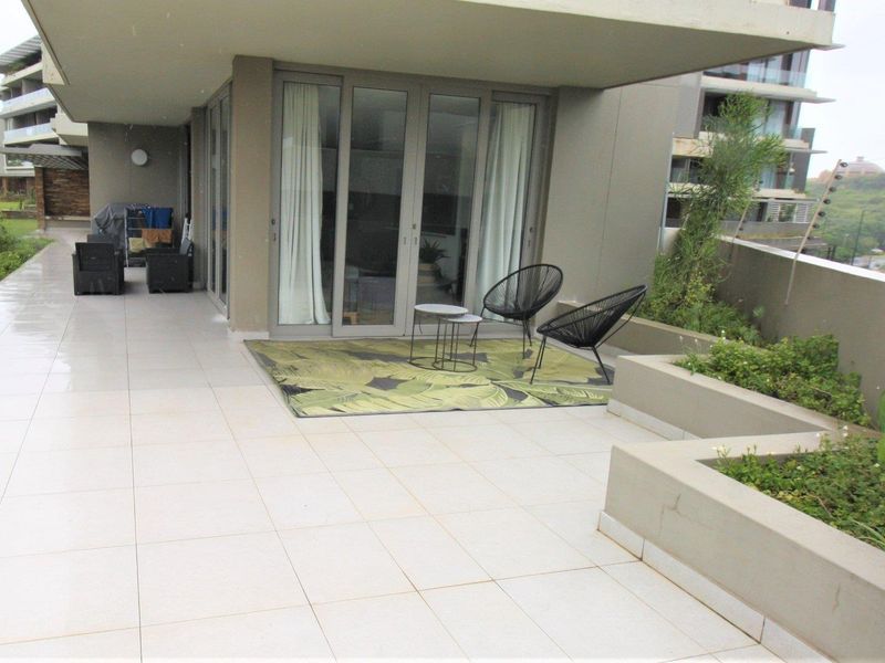 Spacious covered balcony featuring light-toned floor tiles, integrated planter boxes, and large sliding glass doors providing seamless indoor-outdoor flow.