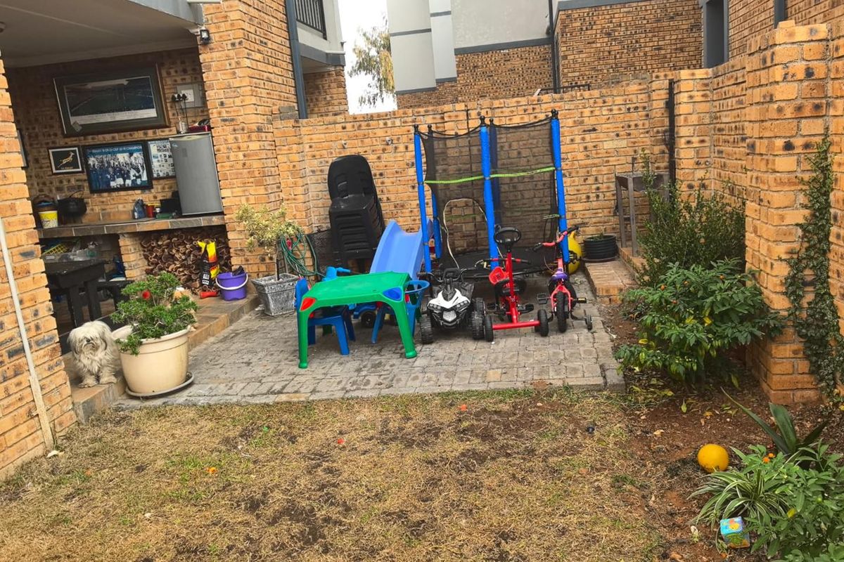A private rear courtyard featuring a paved patio area with a built-in brick braai and a small garden space.
