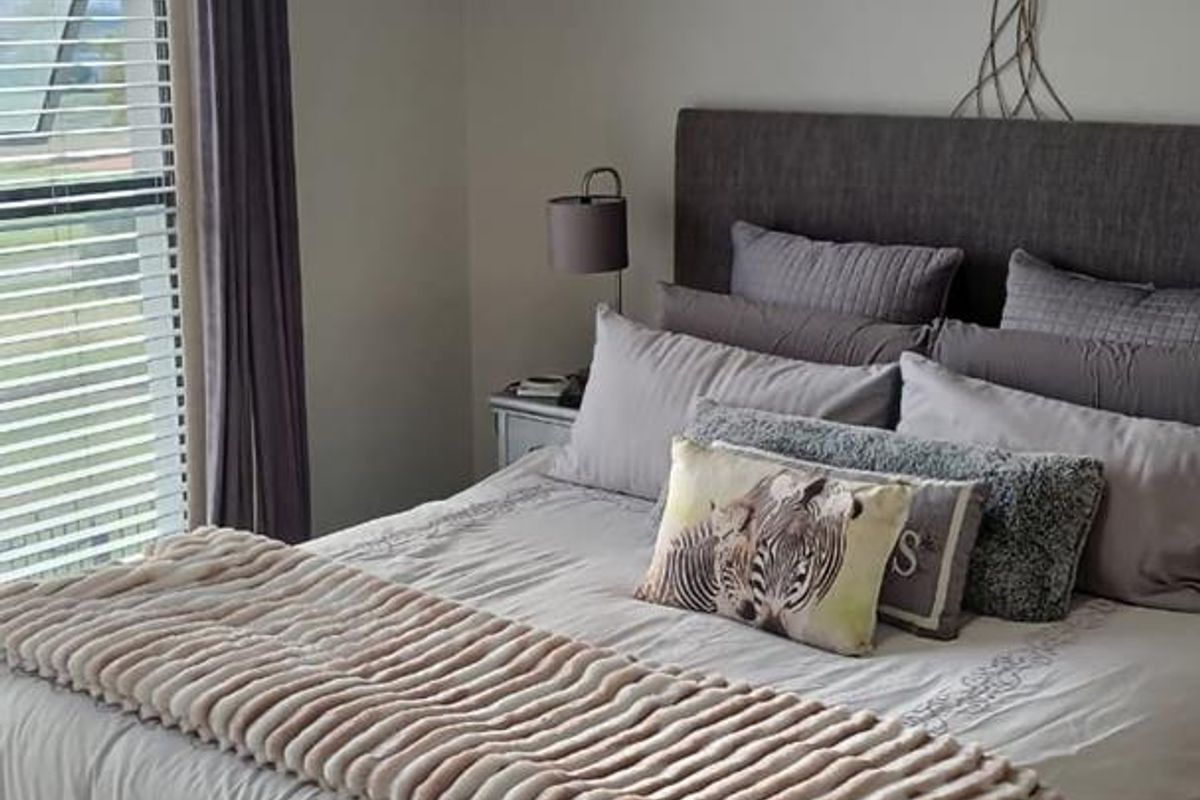 A well-maintained bedroom featuring neutral wall tones, a large window with fitted blinds, and modern curtain tracks.