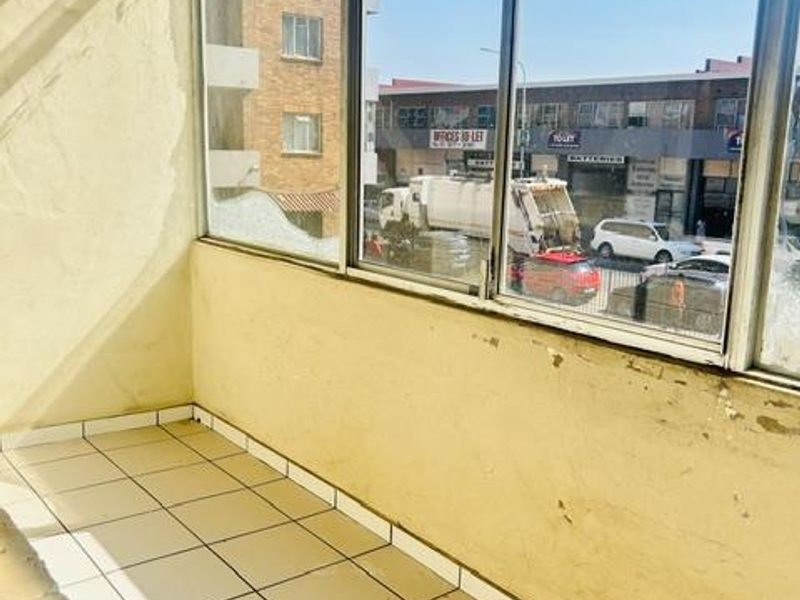 An enclosed balcony area featuring tiled flooring and large aluminium-framed windows, currently in need of maintenance and cosmetic updates.