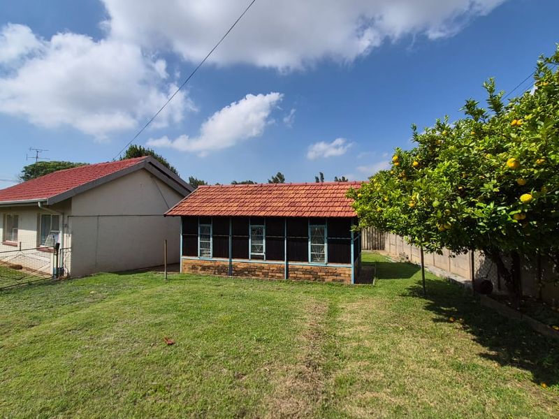 Rear view of the property featuring a secondary outbuilding with terracotta roof tiles, set within a spacious garden area with established fruit trees.