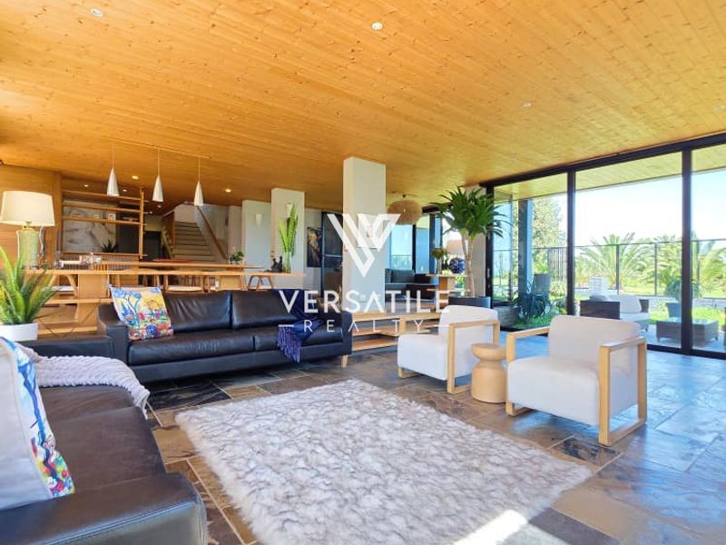 Spacious open-plan living area featuring natural stone flooring, a warm timber-clad ceiling, and expansive floor-to-ceiling glass doors opening to the outdoors.