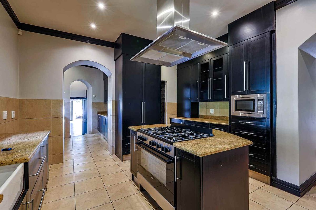 Spacious kitchen featuring dark cabinetry, granite countertops, a central island with a gas hob, and a stainless steel extractor fan.