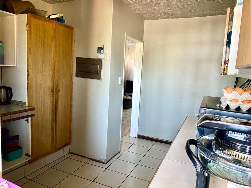 A functional kitchen area featuring tiled flooring, built-in wooden cabinetry, and access to an adjacent room.