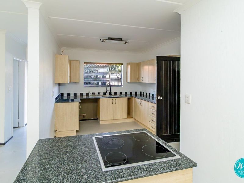 A functional kitchen featuring light wood cabinetry, dark granite-look countertops, a built-in electric cooktop, and a tiled backsplash.