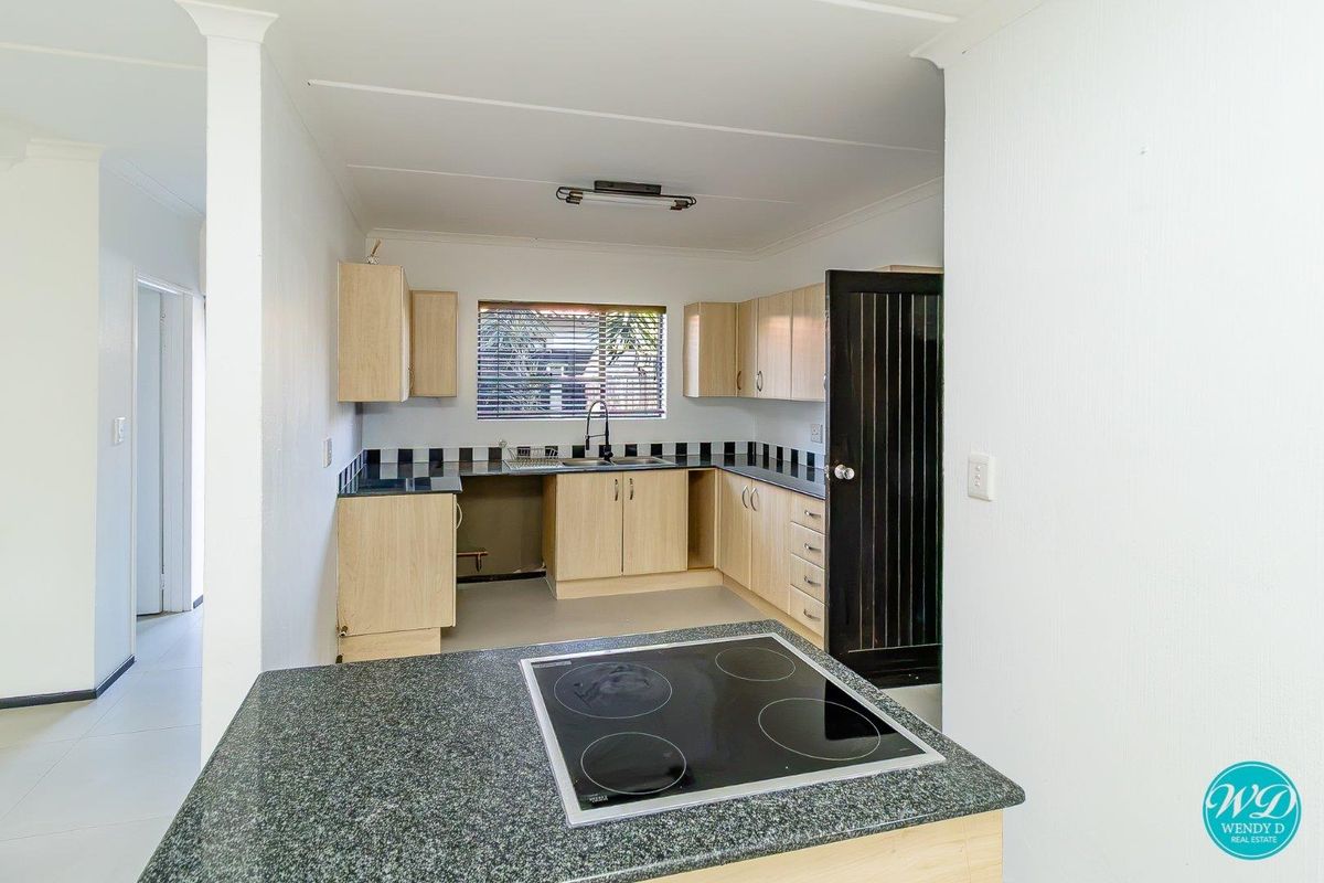 A functional kitchen featuring light wood cabinetry, dark granite-look countertops, a built-in electric cooktop, and a tiled backsplash.