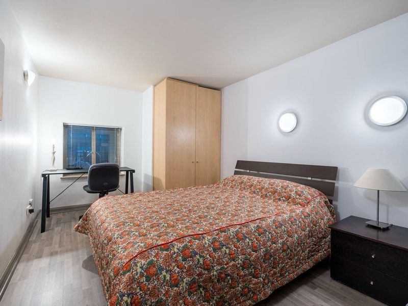 A functional bedroom featuring laminate flooring, a built-in wardrobe, and wall-mounted lighting, providing a practical and well-lit sleeping space.