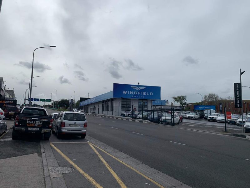 Street-level view of a commercial motor dealership property featuring prominent signage, perimeter fencing, and paved access areas.