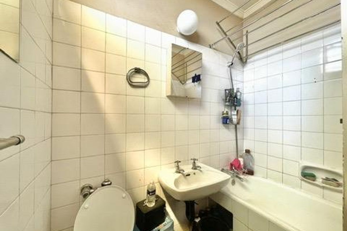 A compact bathroom featuring a standard bathtub, wall-mounted basin, and toilet with white tiled walls and overhead lighting.