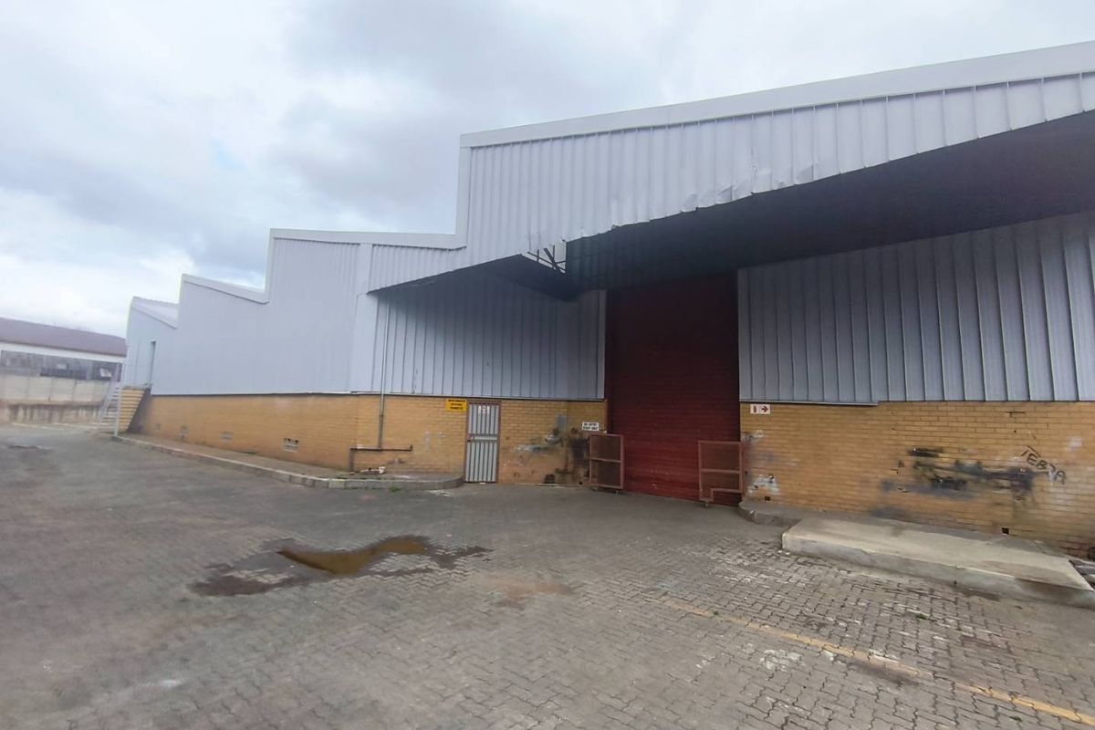 Industrial warehouse exterior featuring corrugated metal cladding, a large roller shutter door, and a paved yard area.