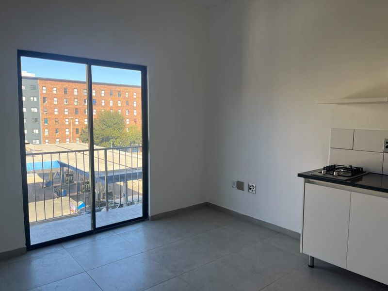 An open-plan living area featuring tiled floors, a compact kitchen with a gas hob, and a sliding door leading to a balcony.
