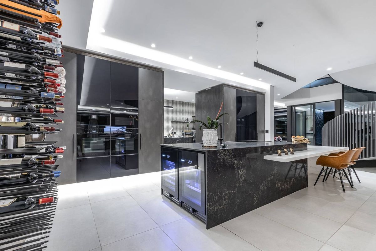 Modern luxury kitchen featuring a large stone island, integrated wine refrigeration, sleek dark cabinetry, and sophisticated recessed lighting throughout the space.